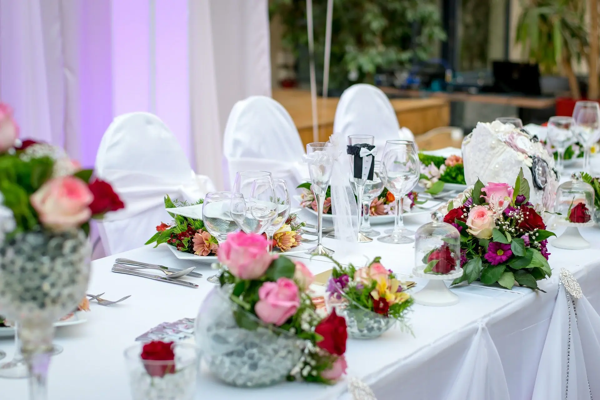 A wedding reception table set with pink and cream roses, glassware and white linen